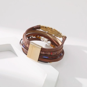 Détail d'un bracelet bohème multicouche en cuir avec plume dorée et perles blanches