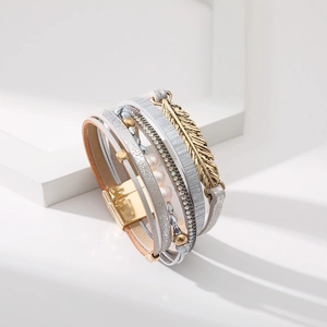 Détail d'un bracelet bohème multicouche en cuir avec breloque plume dorée et fermoir magnétique