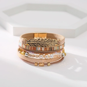 Détail d'un bracelet multicouche en cuir bohème avec plume dorée et fermoir magnétique