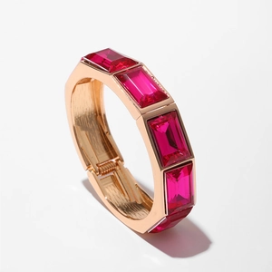 Dettaglio di un bracciale rigido oro rosa con pietre preziose rosse taglio smeraldo