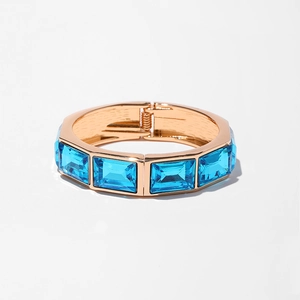 Dettaglio dell'ampio bracciale dorato con grandi cristalli blu rettangolari sfaccettati