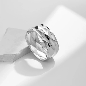 Macro view of wide silver ring featuring a geometric diamond-cut faceted metal texture