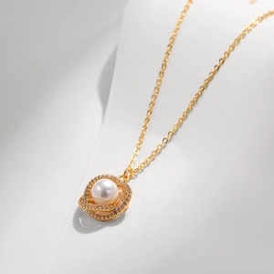 Dettaglio macro della collana d'oro con alone di zirconi e pendente di perla bianca
