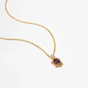 Detailed view of turtle pendant with purple gemstone and zircon inlay on gold necklace