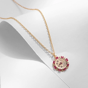 Dettaglio della collana a medaglione solare dorato con zirconi viola e occhio