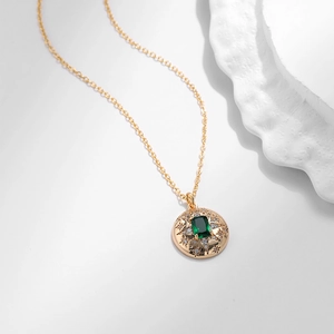 Dettaglio di collana dorata con pietra verde rettangolare e incisioni a forma di stella