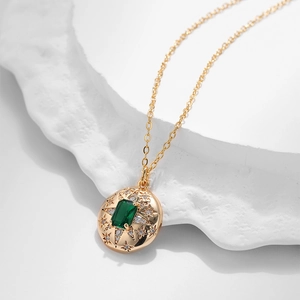 Dettaglio di un ciondolo vintage in oro con pietra verde smeraldo e motivi a stella