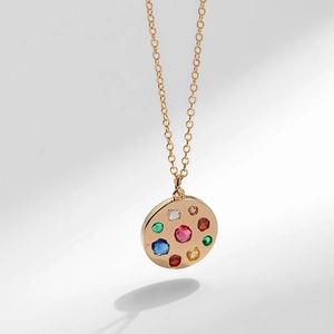 Dettaglio collana dorata con ciondolo circolare impreziosito da gemme colorate e zirconi