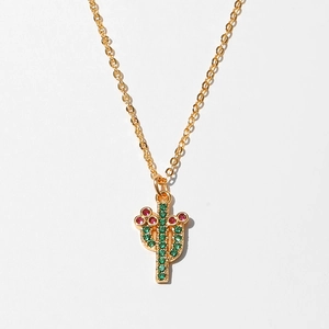 Detail shot of golden necklace with cactus pendant featuring green and pink crystals