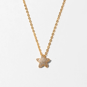 Close-up of golden starfish pendant with sparkling pave crystals on a minimalist chain