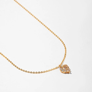 Detailed view of a gold heart pendant with white zircons on a delicate cross chain