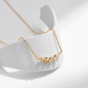 Dettaglio della collana con ciondolo a foglia d'oro e zircone marquise su sfondo sobrio