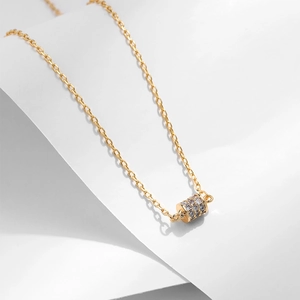 Primo piano di una collana dorata con ciondolo a cilindro decorato con zirconi brillanti