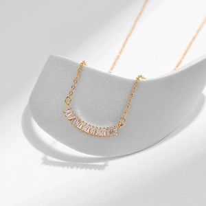 Dettaglio di collana dorata con pendente curvo in zircone su supporto geometrico bianco