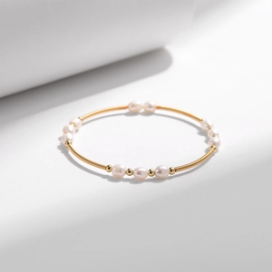Detailaufnahme eines goldenen Armreifs mit Perlen und filigranem Federdraht-Design