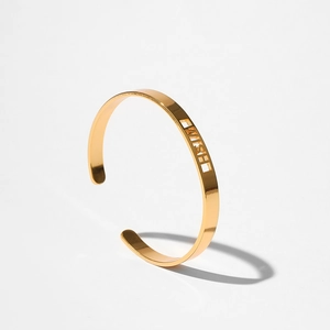 Dettaglio macro del bracciale rigido dorato con scritte WISH intagliate su metallo lucido