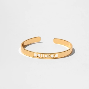 Dettaglio macro del bracciale rigido dorato con incisione traforata della scritta LUCKY