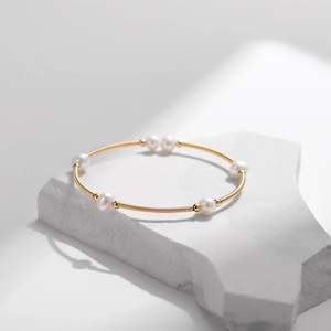 Makroaufnahme des vergoldeten Süßwasserperlen-Armbands auf minimalistischem Graustein