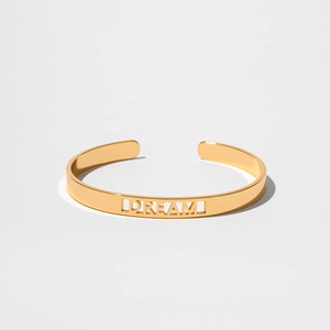 Dettaglio di un bracciale rigido dorato con design a intaglio DREAM minimalista