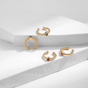 Ensemble de quatre ear cuffs dorés avec zircons verts et rouges sur socle blanc