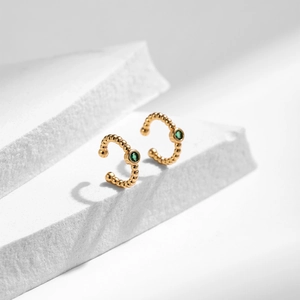 Détail de boucles d'oreilles ear cuff dorées avec zircon vert sur pierre blanche
