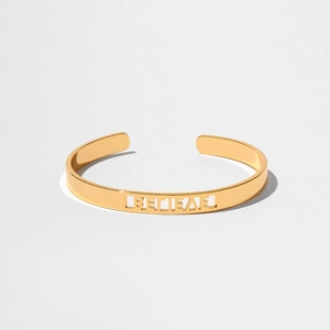 Dettaglio macro del bracciale aperto dorato con scritte BELIEVE traforate di classe