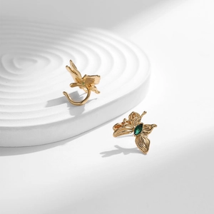 Manchette d'oreille papillon dorée 18K avec zircons verts sur présentoir blanc épuré