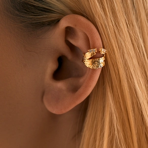 Détail d'un ear cuff doré à texture lave et zircons porté sur oreille sans perçage