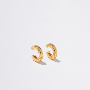 Detail view of gold-plated C-shaped ear clips with fine horizontal textured patterns