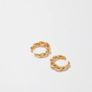 Detailed view of two gold twisted rope ear cuffs on white background with soft shadows