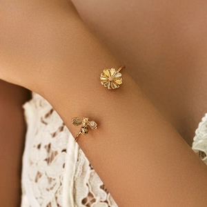 Detail of 18K gold-plated cuff bracelet featuring daisy and bee charms with micro-inlays