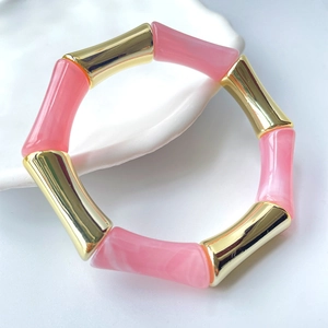 Detailaufnahme des Armbands aus rosa Harz und Goldmetall in Bambusoptik auf Keramik