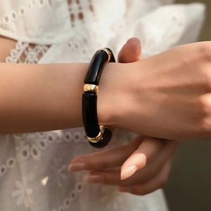 Close-up of bohemian style black resin tube bracelet with gold accent beads on wrist