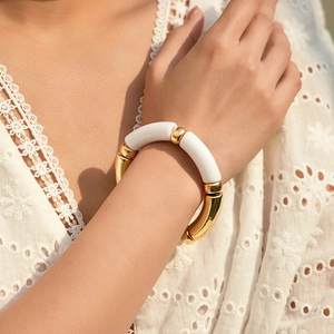 Detail of beaded bracelet with white and gold curved tubes worn on a female wrist