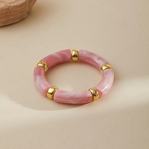 Macro detail of pink marble acrylic bangle with golden spacers on a textured background