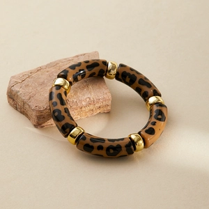 Detail of leopard print resin tubes with gold polished rings on a natural stone background