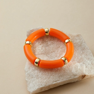 Detail of bamboo-style orange acrylic bracelet on white stone with gold spacers