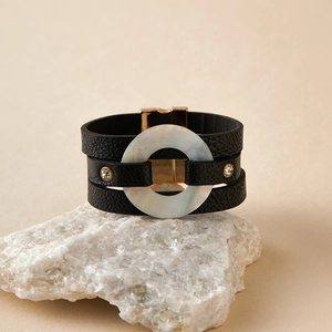 Detalle de pulsera multicapa de cuero negro con anillo de concha y cierre magnético