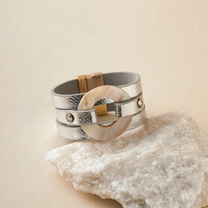 Detalle de pulsera de cuero plateado con cierre magnético dorado y un anillo de resina