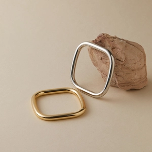 Gepolijste goud- en zilverkleurige vierkante armbanden op natuurlijke steenstructuur
