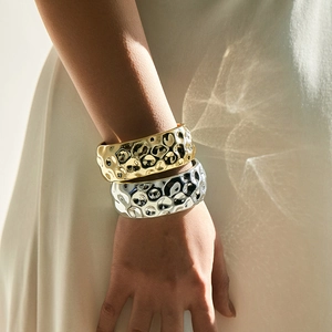Gouden en zilveren brede gehamerde armbanden met lava-textuur om een pols gedragen