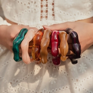 Set di bracciali in acrilico colorato ondulato mostrati su abito in pizzo bianco
