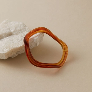 Détail du bracelet en résine ambre marron foncé au design ondulé organique sur pierre