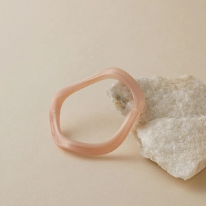 Détail d'un bracelet acrylique ondulé rose sur une pierre blanche en décor minimaliste
