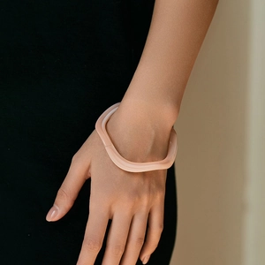 Gros plan d'un bracelet acrylique ondulé rose pâle porté au poignet pour un style moderne