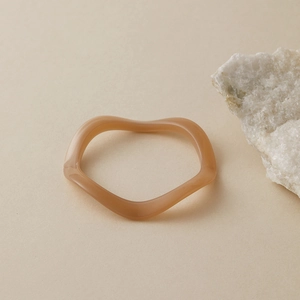 Gros plan du bracelet ondulé en résine caramel sur fond beige avec cristal décoratif