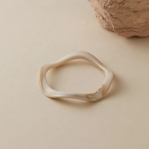 Gros plan d'un bracelet acrylique ondulé avec texture marbre crème sur fond minéral