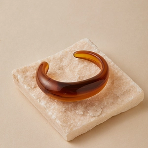 Dettaglio del bracciale aperto in acrilico ambra traslucido con texture irregolare su pietra