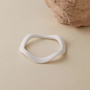 Détail d'un bracelet minimaliste blanc en résine ondulée posé sur pierre naturelle