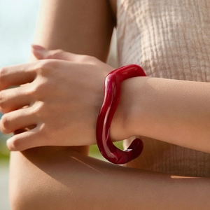 Bracciale rigido aperto irregolare in acrilico rosso scuro con finitura in resina sul polso